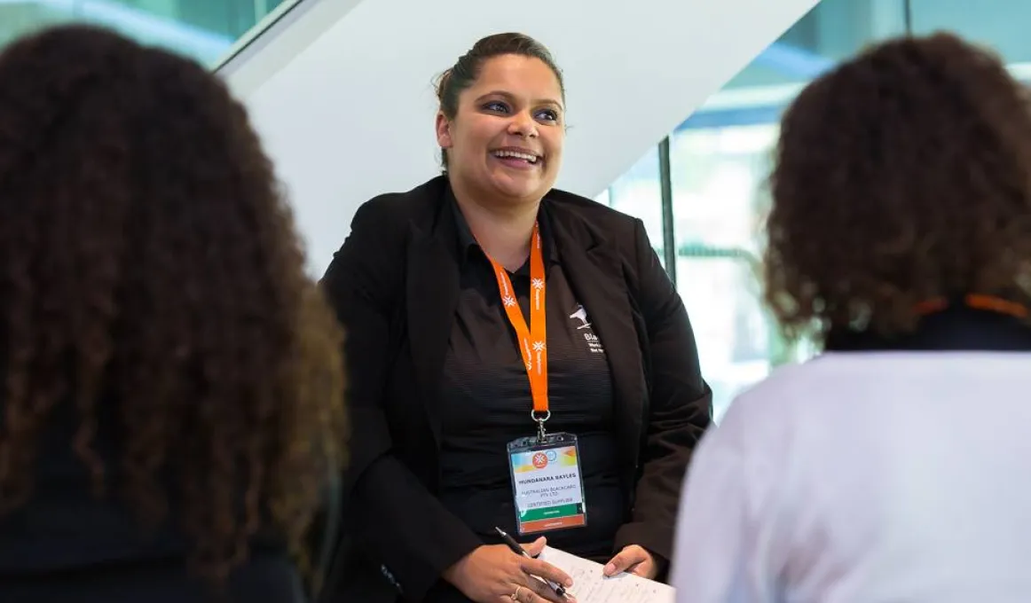 Indigenous woman and trainer Mundanara Bayles, sits in front of two people who face her and with their backs to camera