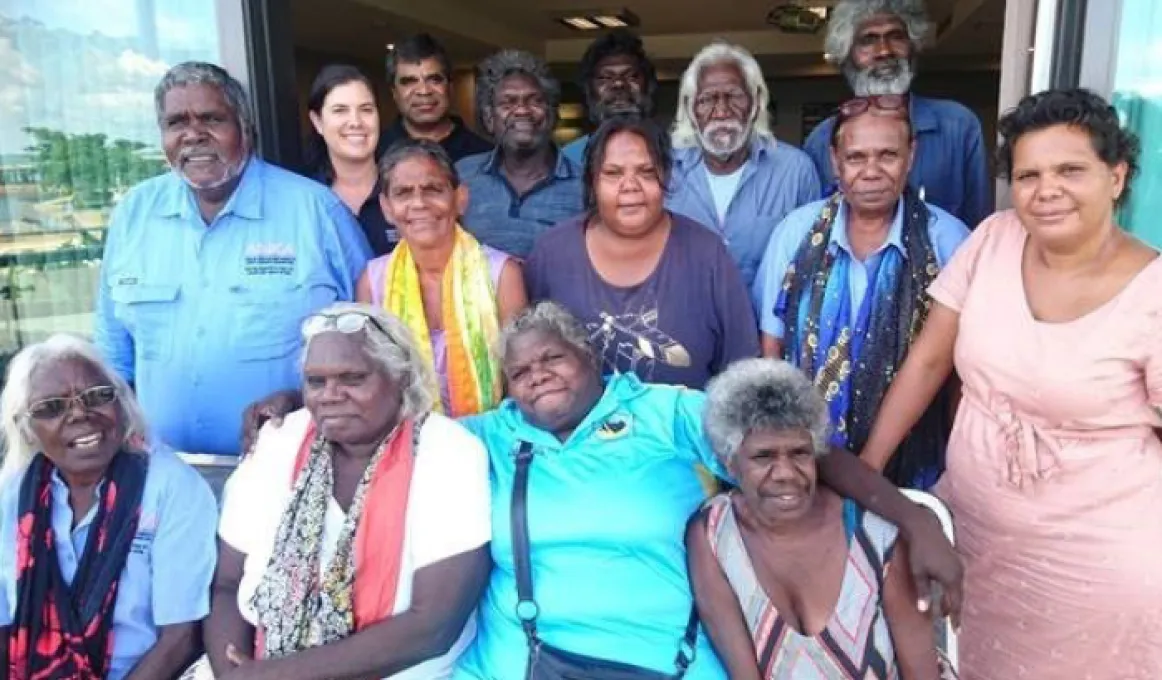 Group of people sitting and standing in rows in a doorway looking at the camera. They wear different coloured clothing.