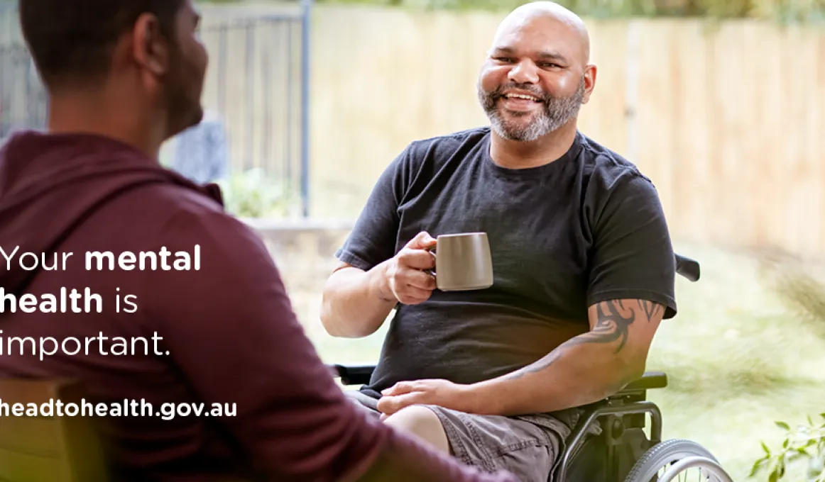 Two men sit opposite each other, oine in a wheel chair and holding a mug. He wears a dark t-shirt the other a maroon hoodie. Overlaid are the words: your mental health is important. headtohealth.gov.au. In the background is a pale coloured fence.