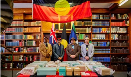 Four men stand behind a table under an Aboriginal flag