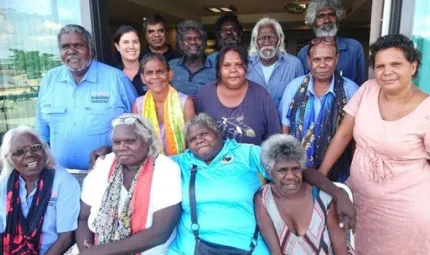 Group of people sitting and standing in rows in a doorway looking at the camera. They wear different coloured clothing.