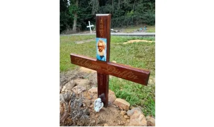 A brown cross sits on a grave. It includes the name and photo of the deceased.