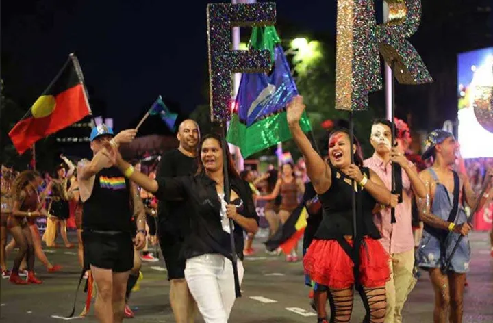 A group of people holding the Aboriginal and Torres Strait Islander flags march in front of the First Nations float during Sydney’s Mardi Gras parade. Credit: SBS