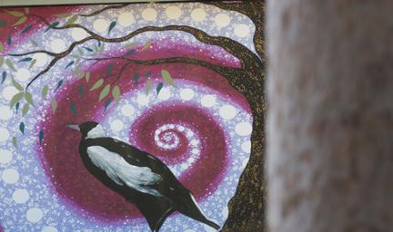A black and white bird stands next to the trunk of a tree. In the background is a white and moroon swirl made up of circles and dots. In the foreground is another tree trunk.