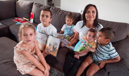 A woman and 5 children sit on a brown couch and look at the camera.